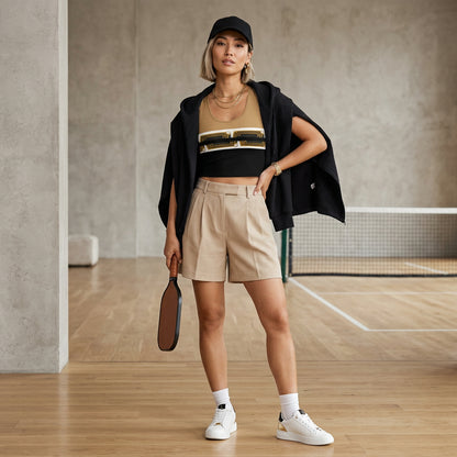 An Asian lady with short blond hair is wearing a  nude and black crop top and beige shorts at pickle bball court holding a racket.
