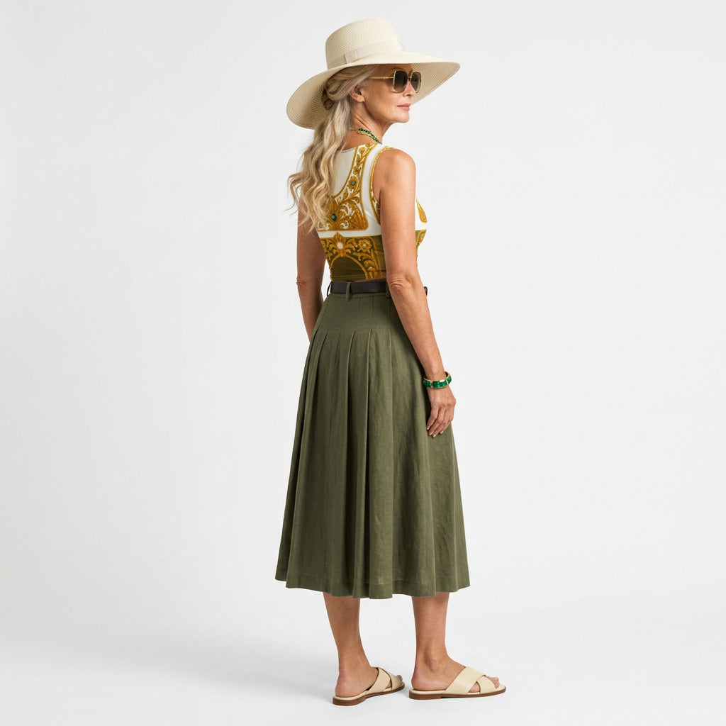 Full picture of a senior model in sunglasses wearing ARTEMI ARTELIA's crop Top coordinated with green skirt, cream flat sandals and a hat. The top has Baroque filigree design print with emerald embellishments on white and olive green. 