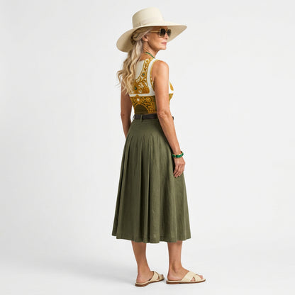 Full picture of a senior model in sunglasses wearing ARTEMI ARTELIA's crop Top coordinated with green skirt, cream flat sandals and a hat. The top has Baroque filigree design print with emerald embellishments on white and olive green. 