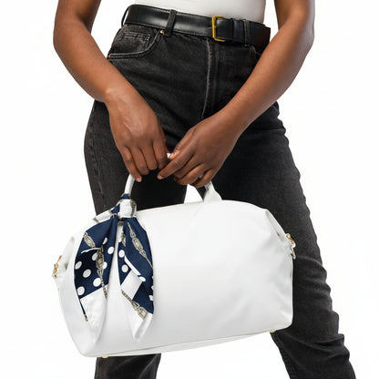 Person holding a white handbag with a blue and white polka dot scarf draped over it, wearing black jeans and a white top.