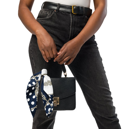 Person holding a black handbag with a polka dot scarf draped over it on a white background