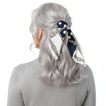 Person with silver semi-long hair, photographed from behind, wearing a navy blue scarf with white polka dots and Art Deco jewel motifs tied as a half-up hair wrap.