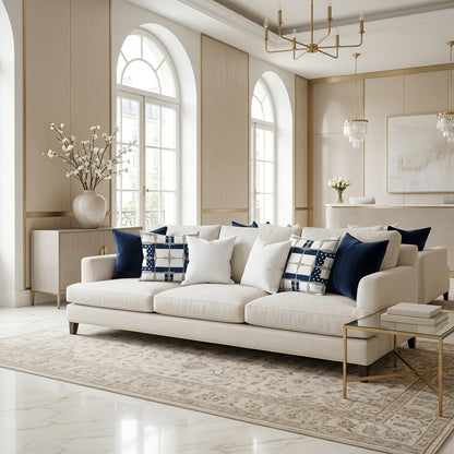 A cream-colored three-seater sofa in a bright, modern living room with arched windows, patterned navy and white throw pillows, and a beige rug.