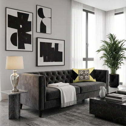 A rectangular throw pillow with a black and white geometric central design and black corner triangles on a pale yellow background, resting on a textured blue and beige throw blanket on a beige sofa next to a green houseplant.