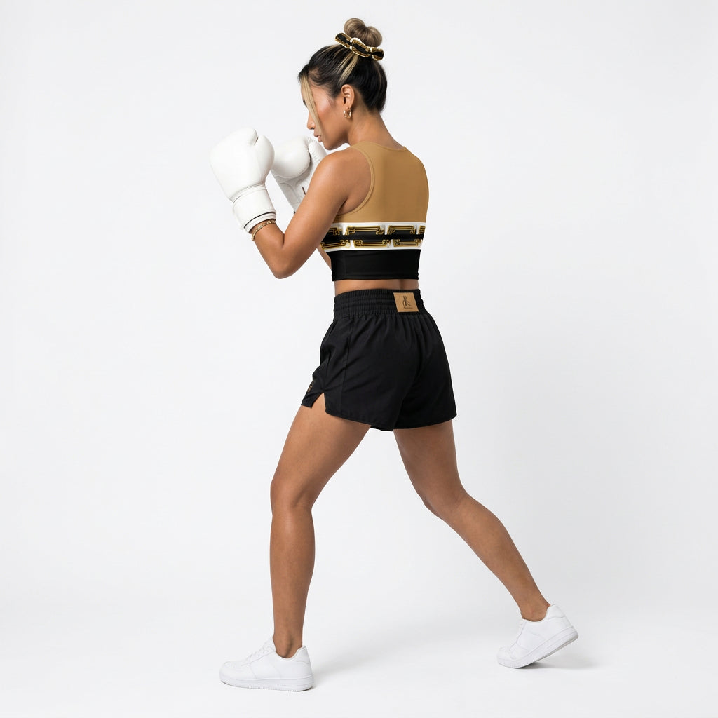 A cropped tank top with a color-blocked design featuring a tan upper section, a white middle band with a black and gold geometric pattern and pearl-like accents, and a solid black lower section.