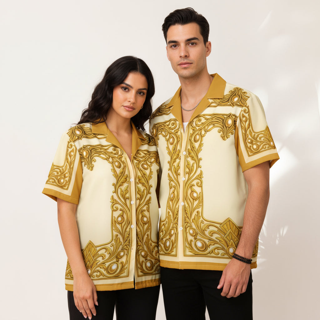 A man with curly brown hair wearing a cream-colored short-sleeve button-up shirt with ornate gold baroque-style embroidery, styled over a white undershirt.