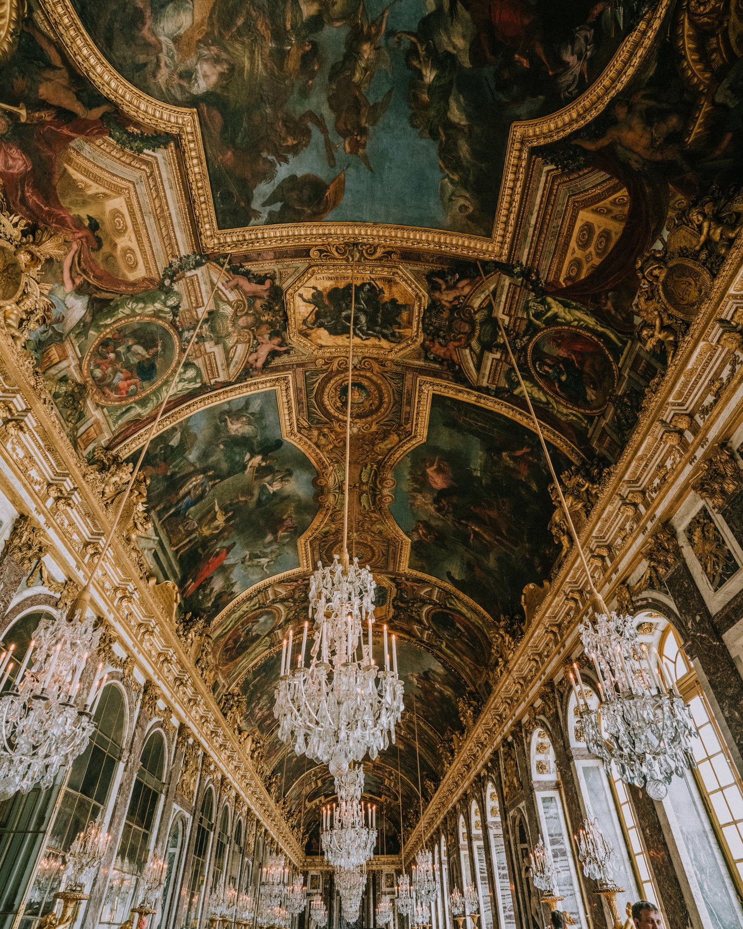 The aged frescoes, crystal chandeliers and gold leaf-covered trim that cover the ceiling of long hallway in the Palace of Versaille. French Baroque style at its most extravagant.